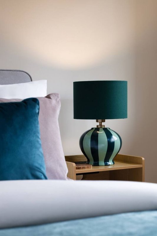 Bedroom detail with blue cushion, striped table lamp and wooden bedside table