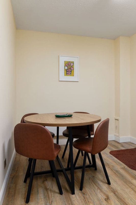 Dining area with round wooden table, two brown leather chairs, and framed artwork on wall