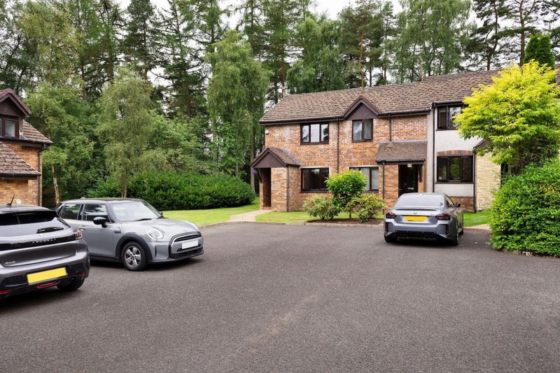 Brick residential property with driveway, parked cars, and surrounding woodland garden