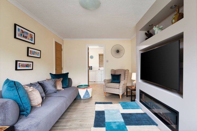 Open-plan living room with gray sofa, blue cushions, wall-mounted TV, fireplace, and modern furnishings