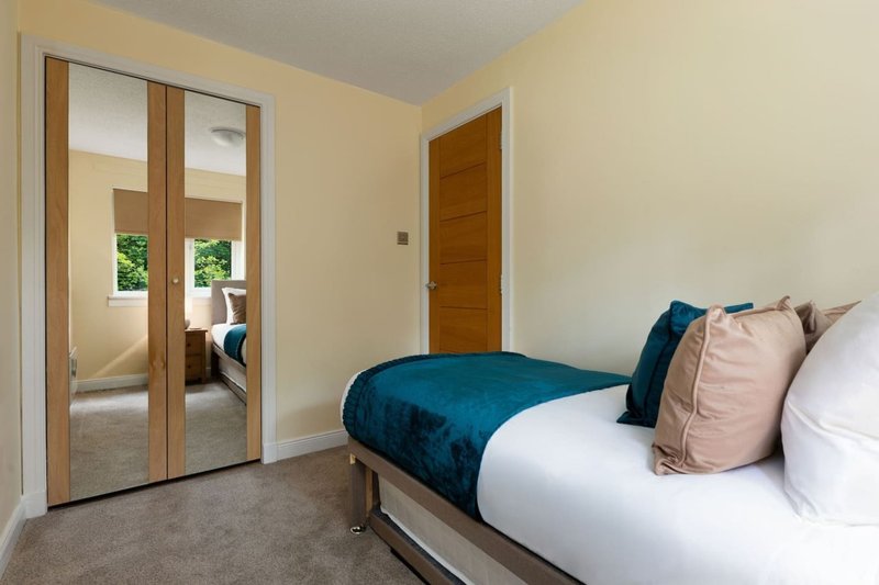 Modern bedroom with double bed, teal throw, decorative pillows and mirrored wardrobe doors