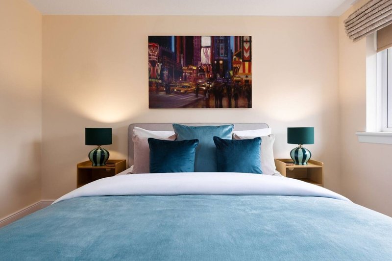 Modern bedroom with double bed, blue bedding, teal pillows and wall-mounted artwork