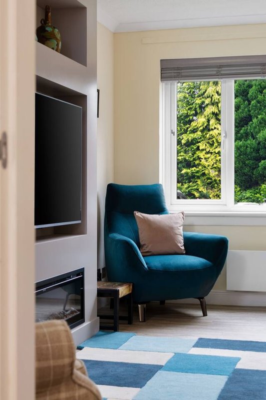 Modern living room with teal armchair, wall-mounted TV, large windows overlooking garden