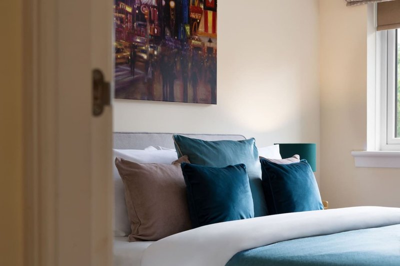 Bedroom with double bed, teal and grey cushions, framed city artwork above headboard