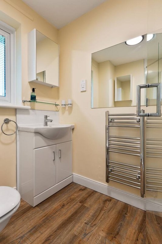 Modern bathroom with white sink vanity, mirror, heated towel rail and wooden flooring