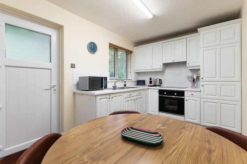 Modern kitchen with white cabinetry, black oven, and wooden dining table in foreground