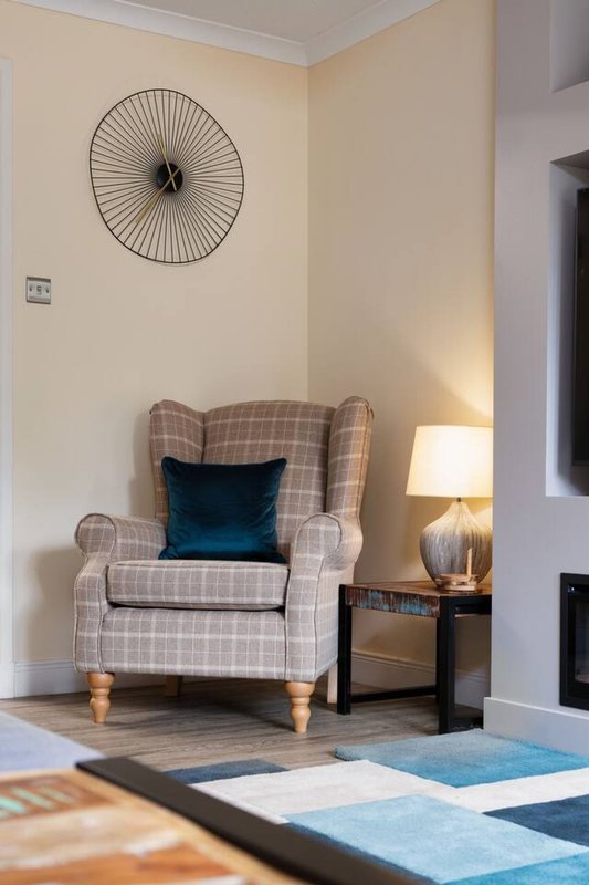 Cozy corner with upholstered armchair, side table, lamp, and decorative wall clock