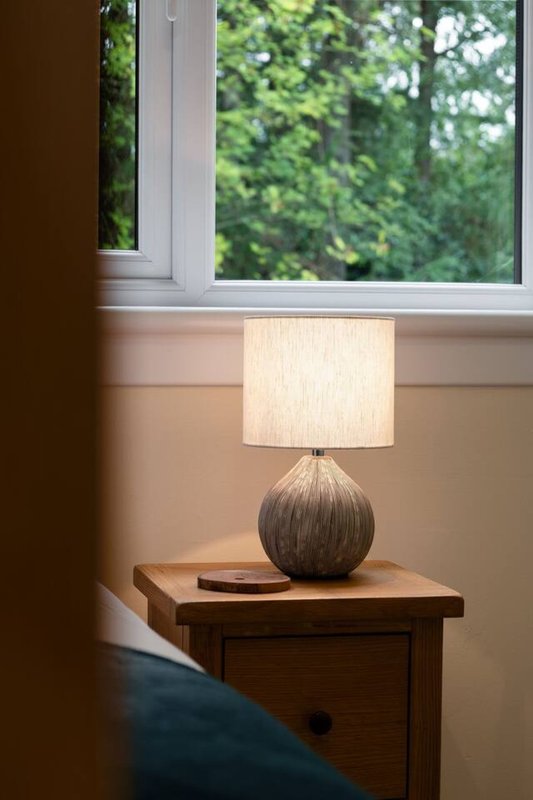 Wooden bedside table with spherical lamp and cream shade, window with garden view