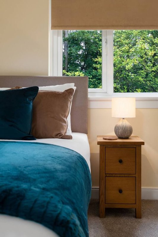 Bedroom with teal duvet, grey headboard, wooden nightstand and garden view