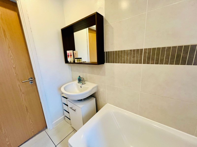 Modern bathroom with white sink, black-framed mirror, storage drawers and white bathtub