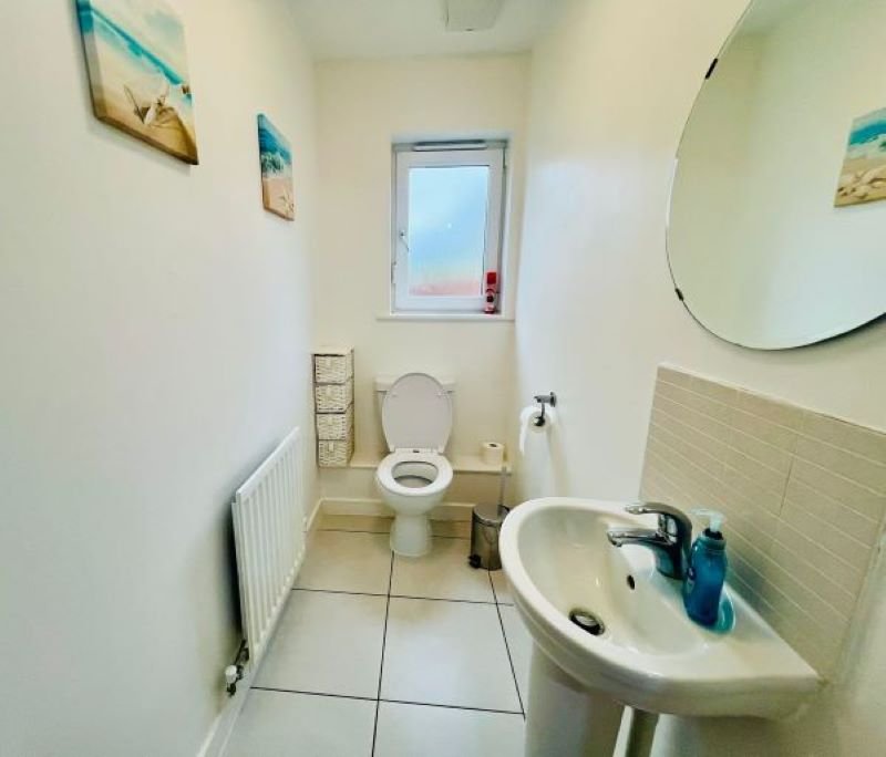Small bathroom with toilet, sink, mirror, window and beige tile flooring