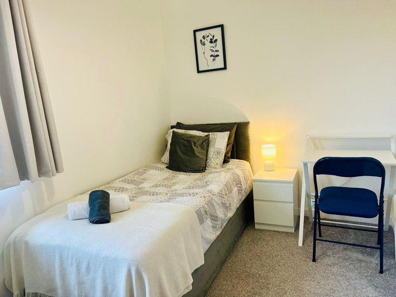 Bedroom with single bed, bedside lamp, wall art, folding chair, and curtains