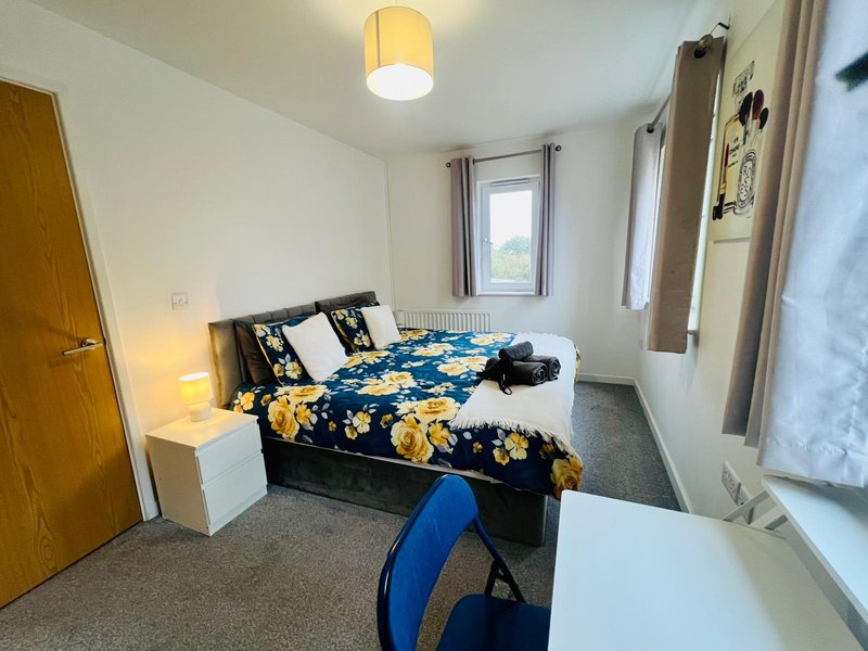 Bedroom with double bed, yellow floral bedding, wooden door, window and desk area