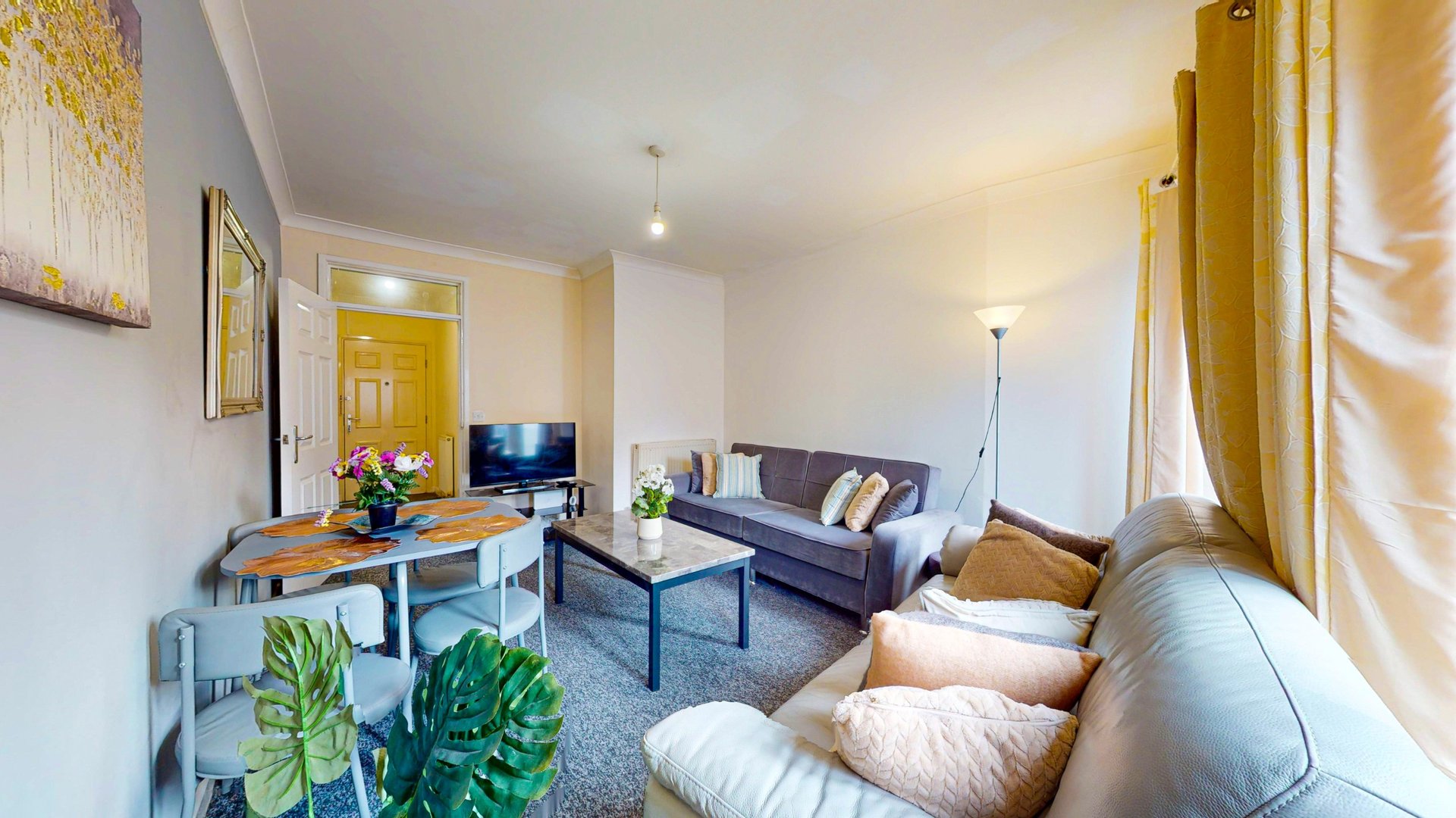 Open-plan living room with sofa, armchair, desk, TV, plants and yellow curtains