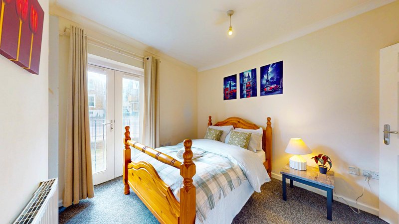 Bright bedroom with wooden bed frame, striped bedding, wall art, and balcony access
