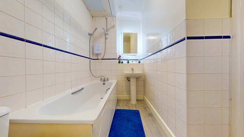 Narrow bathroom with white tile walls, blue stripe detail, sink, bathtub and blue mat