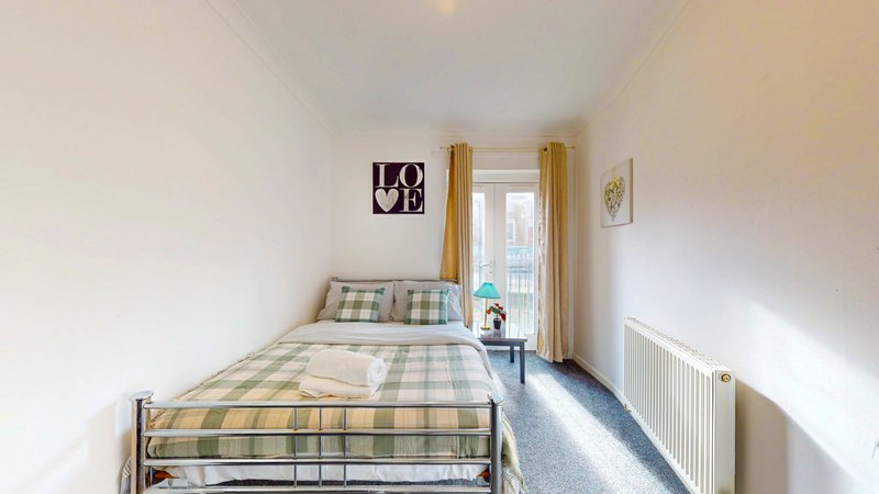 Bright bedroom with single bed, checkered bedding, window with curtains and radiator