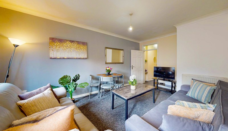 Open-plan living room with sofas, dining table, TV, artwork and potted plants