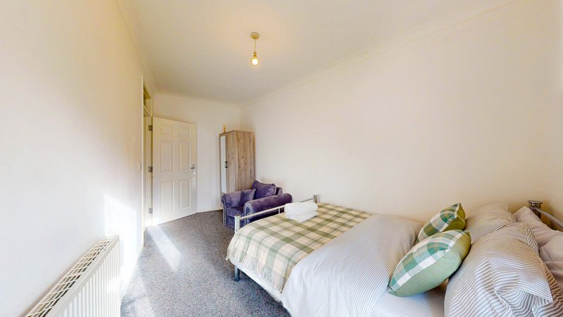 Bright bedroom with double bed, purple armchair, wooden door and grey carpet
