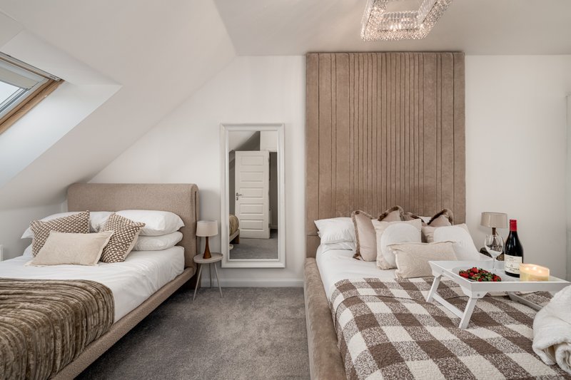 Attic bedroom with two beds, neutral bedding, wine bottle on table, skylights