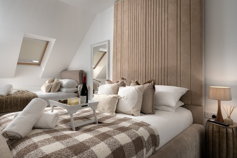 Bright bedroom with double bed, cream pillows, plaid bedding, and floor-to-ceiling curtains