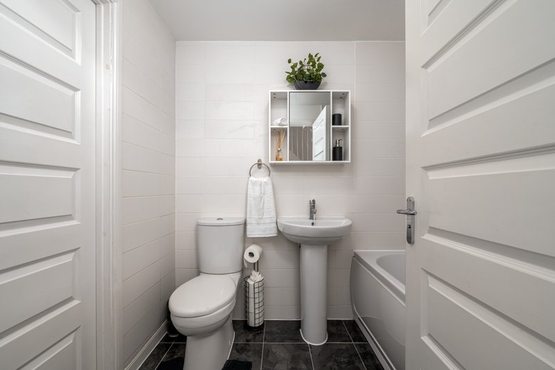 Clean modern bathroom with toilet, pedestal sink, wall-mounted storage and black tile floor