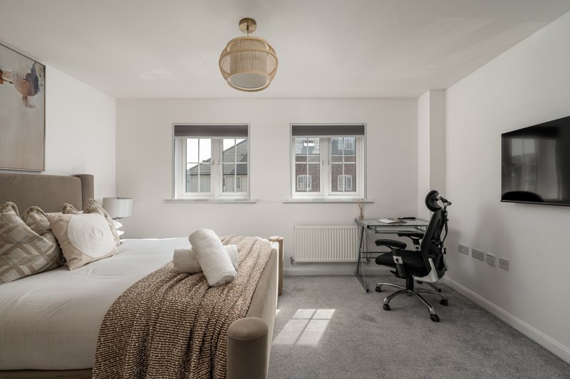 Bright modern bedroom with double bed, desk chair, wall-mounted TV and windows