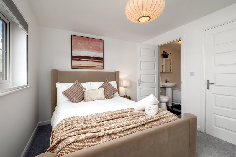 Modern bedroom with double bed, cushions, ensuite bathroom visible through open door