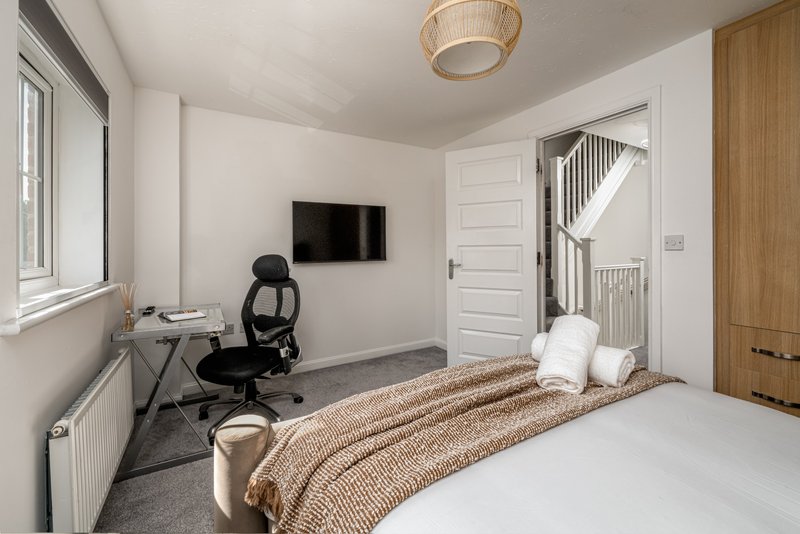 Modern bedroom with double bed, work desk, black chair and wall-mounted TV