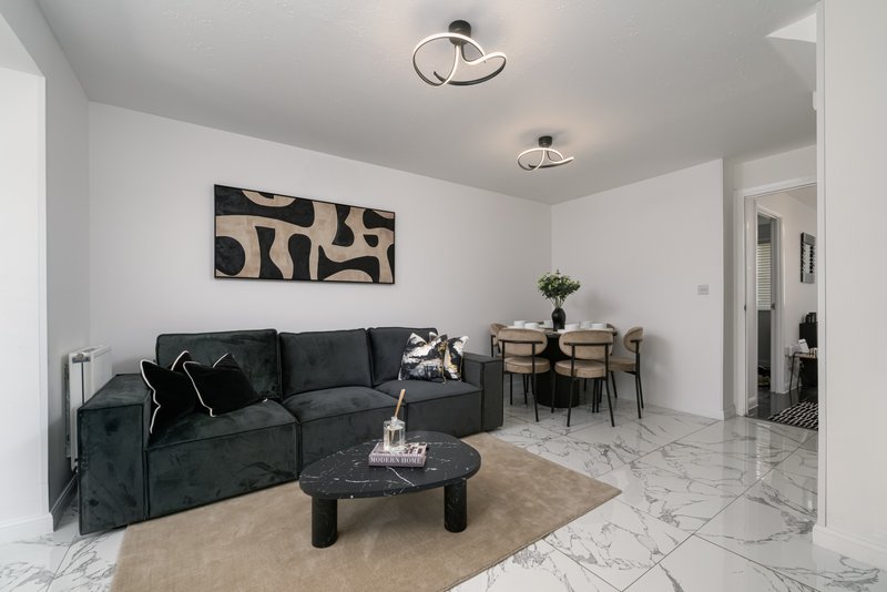 Modern living room with black sectional sofa, marble flooring, dining table and abstract wall art