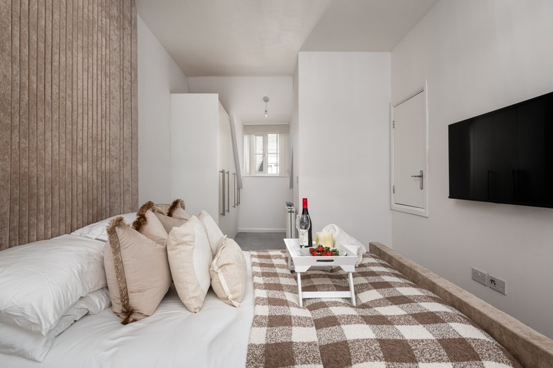 Modern bedroom with double bed, multiple pillows, wall-mounted TV and small side table