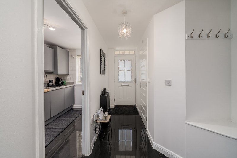 Bright hallway with kitchen door, coat hooks, pendant light and dark flooring