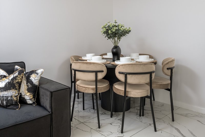 Modern dining area with round table, wooden chairs, black vase with white flowers, and dark sofa