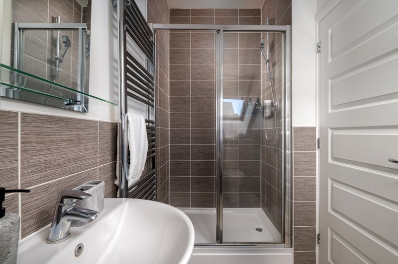 Modern bathroom with brown tile walls, white sink, shower enclosure and mirror