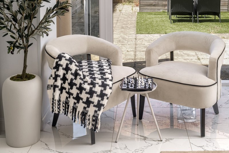 Two cream curved armchairs with black and white patterned throw on patio overlooking garden