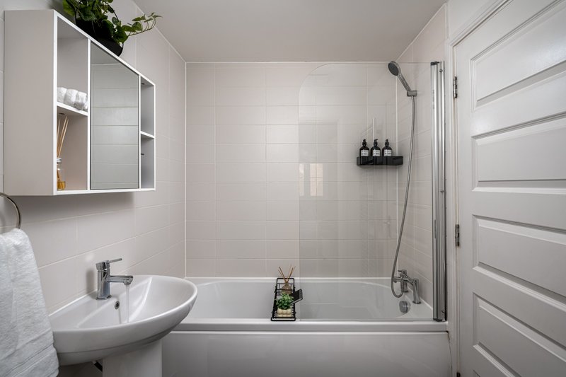 Modern bathroom with white tiles, bathtub, sink, mirror cabinet and shower enclosure