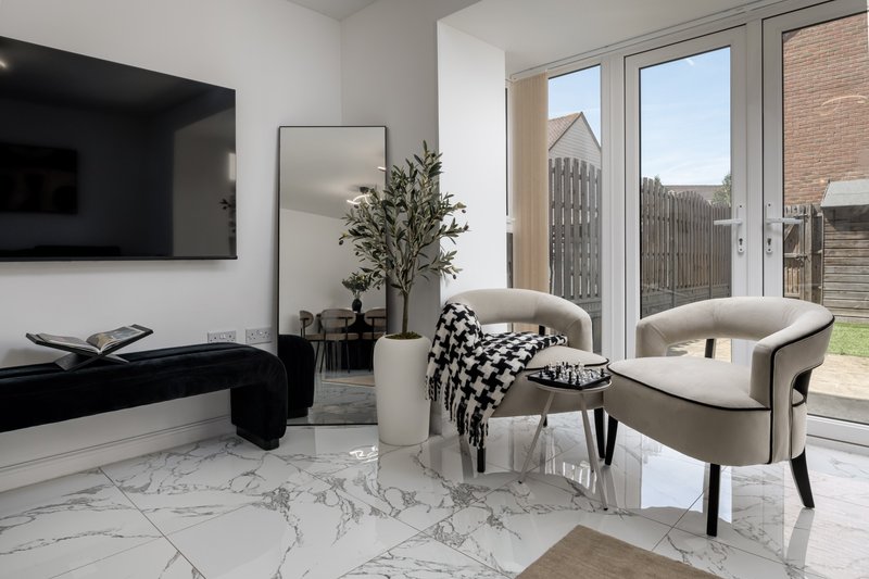 Modern living room with marble flooring, cream armchair, TV, potted plant and garden views