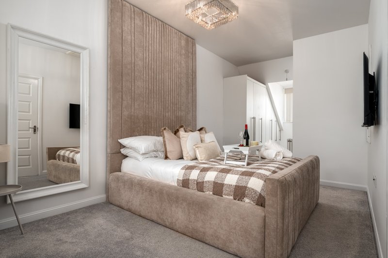 Modern bedroom with upholstered bed, neutral tones, ensuite access and wall-mounted TV