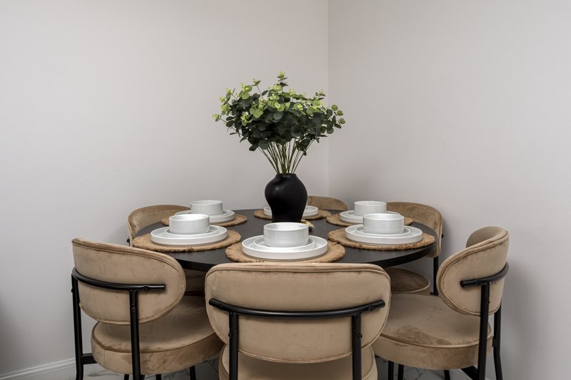 Round dining table with four upholstered chairs, place settings, and floral centerpiece