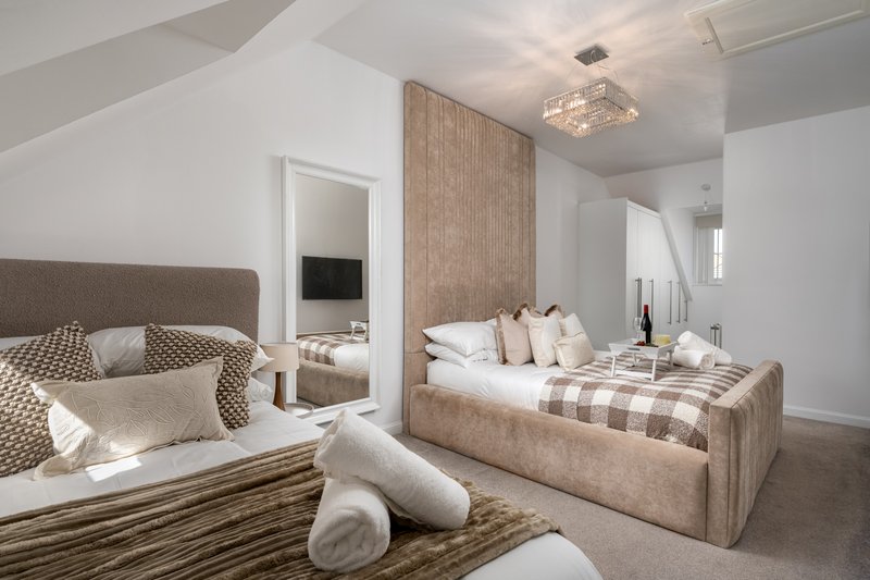 Modern bedroom with two upholstered beds, neutral furnishings, mirror, and contemporary lighting