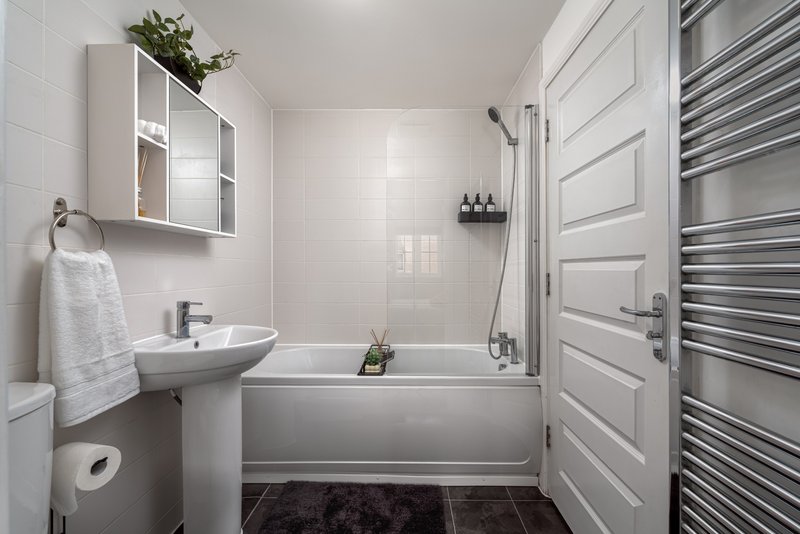 Modern bathroom with pedestal sink, bathtub, white wall cabinets and heated towel rail
