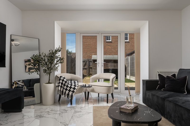 Modern living room with black and white furnishings, marble flooring, and glass doors overlooking garden