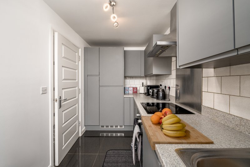 Modern galley kitchen with gray cabinetry, stainless steel appliances, and counter with fresh fruit