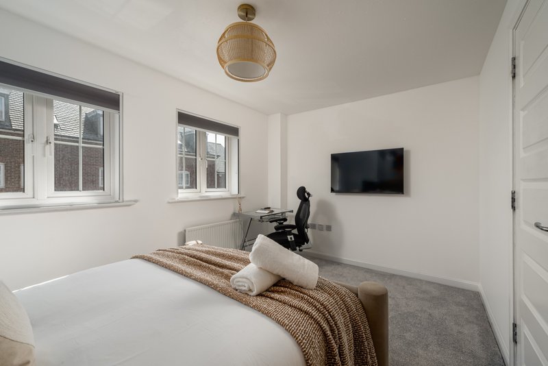 Modern bedroom with white bed, woven pendant light, wall-mounted TV and windows