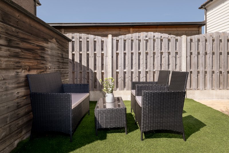 Outdoor patio seating area with two black wicker armchairs, small table, and white picket fence