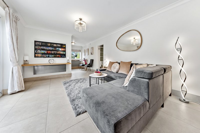 Modern open-plan living room with gray sectional sofa, light tile flooring, and wall-mounted TV