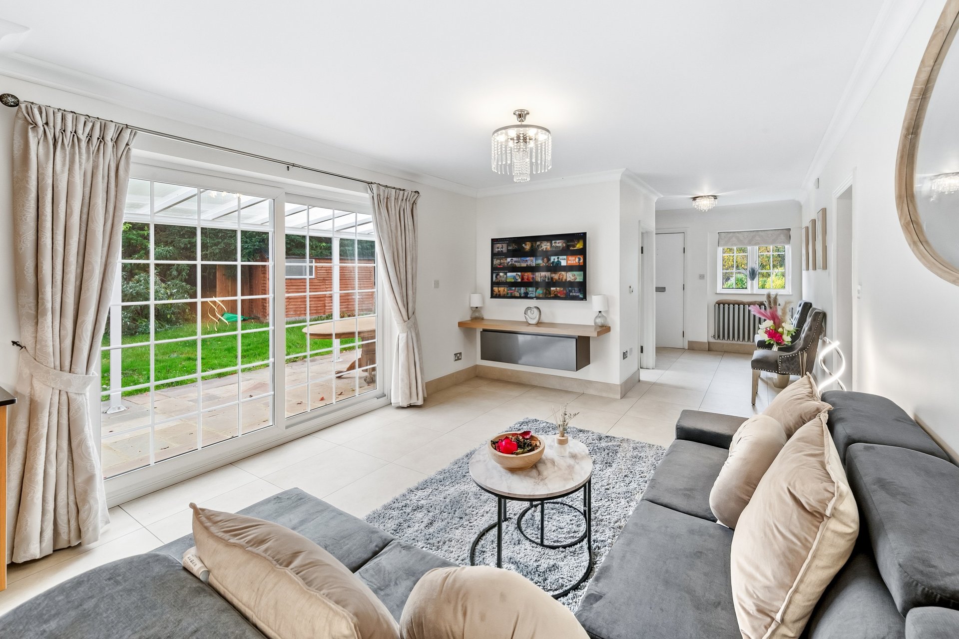 Bright living room with grey sofa, large windows, TV unit, and garden view