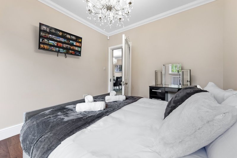 Bedroom with double bed, dark headboard, white pillows, wall-mounted shelving and crystal chandelier