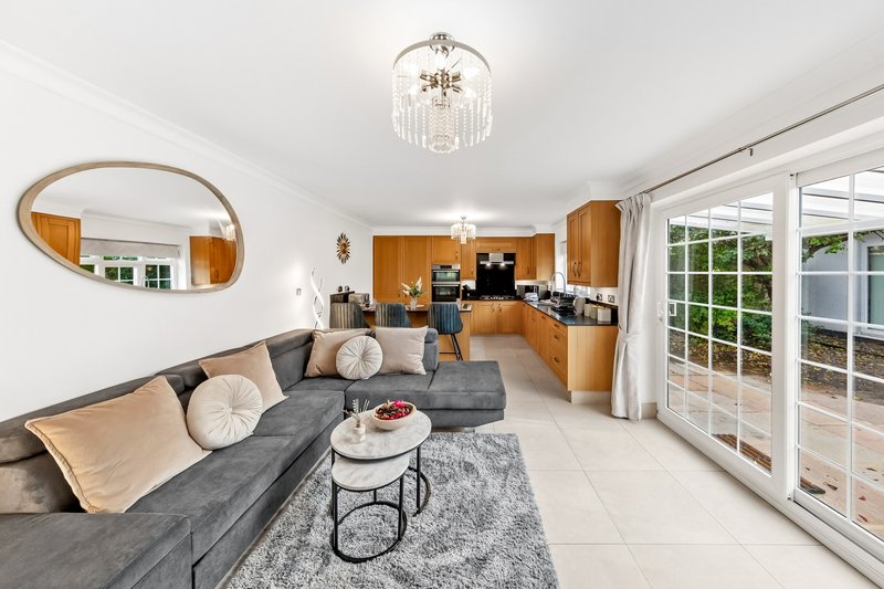 Open-plan living room with gray sofa, wooden kitchen, oval mirror and glass doors to patio
