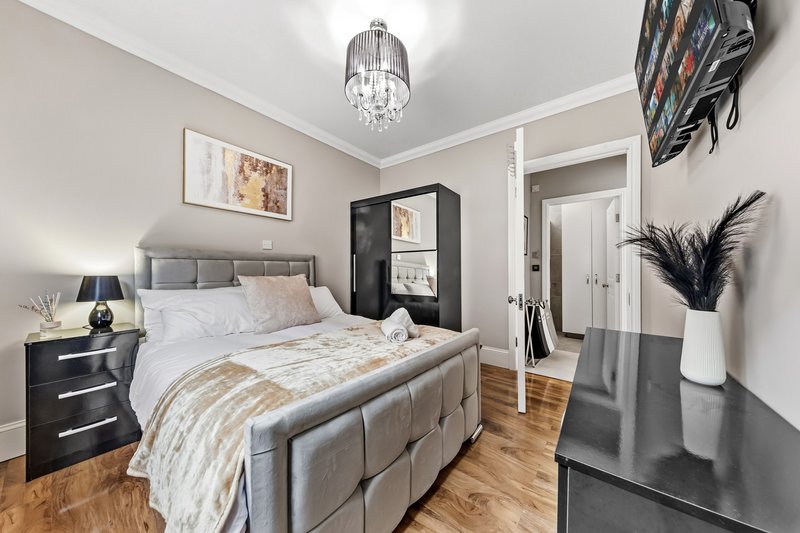 Modern bedroom with gray upholstered bed, wooden flooring, black nightstand, and pendant lighting.